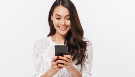 a woman in a white sweater is smiling while looking at her phone